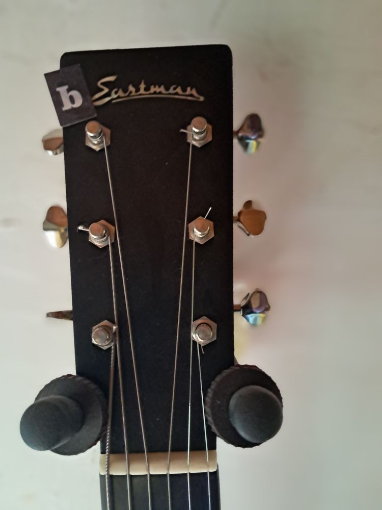 The headstock of an Eastman acoustic guitar with a letter "b" fridge magnet stuck on to read "bEastman"