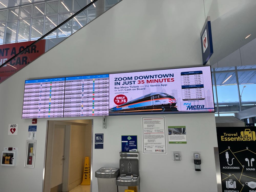 An LED screen advertising Metra's limited airport service next to a screen of upcoming flights.