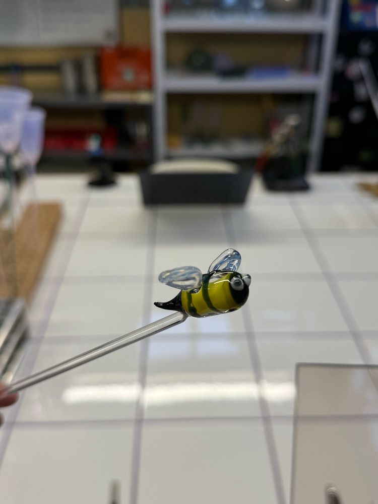 A glass bee on the end of a clear rod. It has large cartoonish eyes and very translucent white wings.
