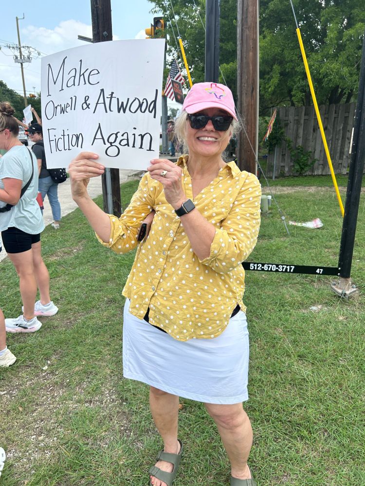 At the Pflugerville TX No Kings Rally today. Woman holding a sign that says, “Make Orwell & Atwood fiction again”