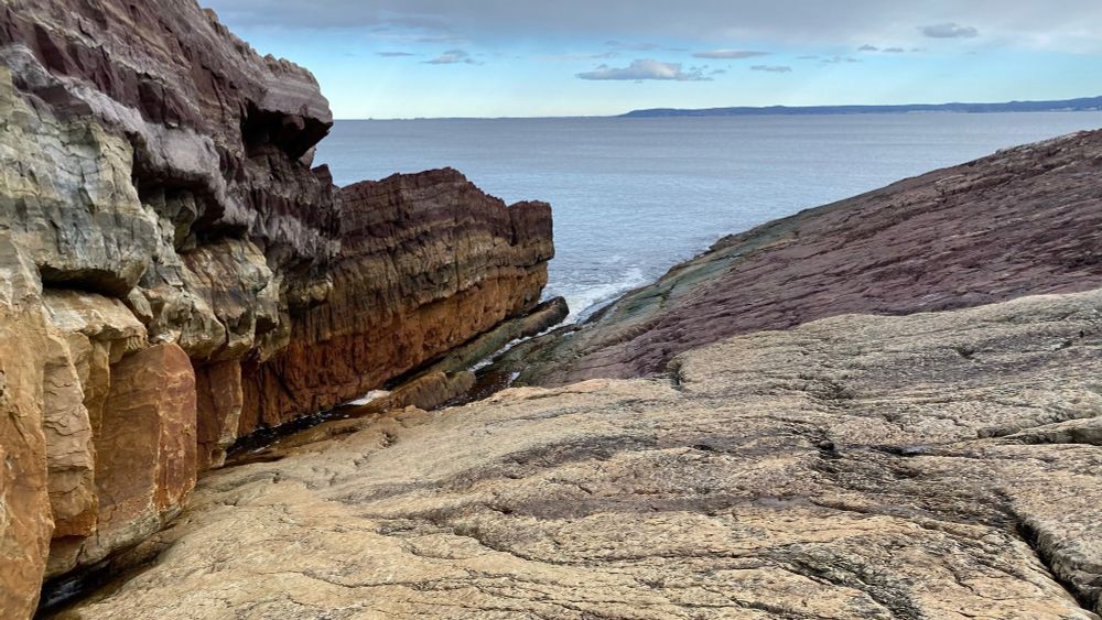 multi-coloured sedimentary rock sloping toward a triangle-shaped wedge of visible ocean