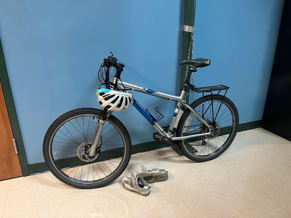 A hardtail mountain bine against a blue wall. It’s in a school stairwell. 