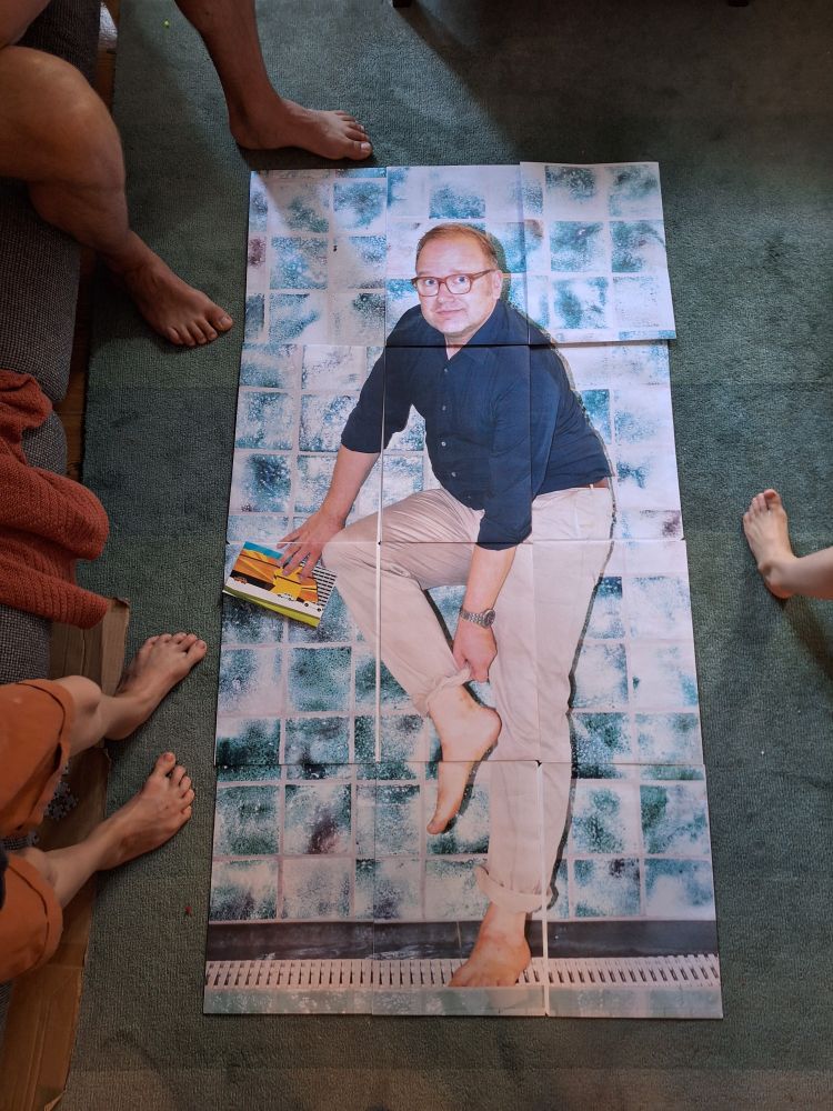Ein Foto von Till Raether, vergrößert auf 12 DIN A3 Seiten, liegt auf einem Teppich. 