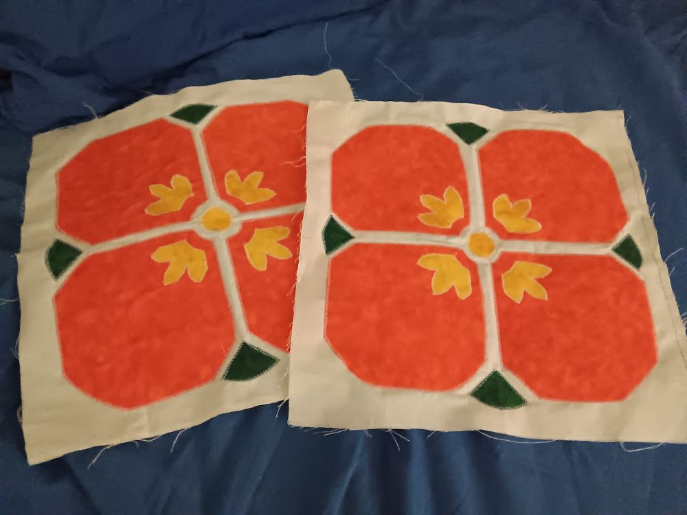 Two orange poppy quilt panels like the one above, lying on a dark blue sheet.