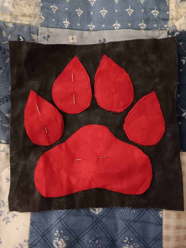 A red wolf pawprint, partially appliqued on a square of dark gray fabric.