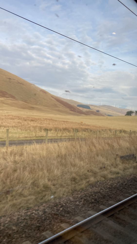 A view from a train crossing the Lake District. Fields of grass and hills into the distance with windmills