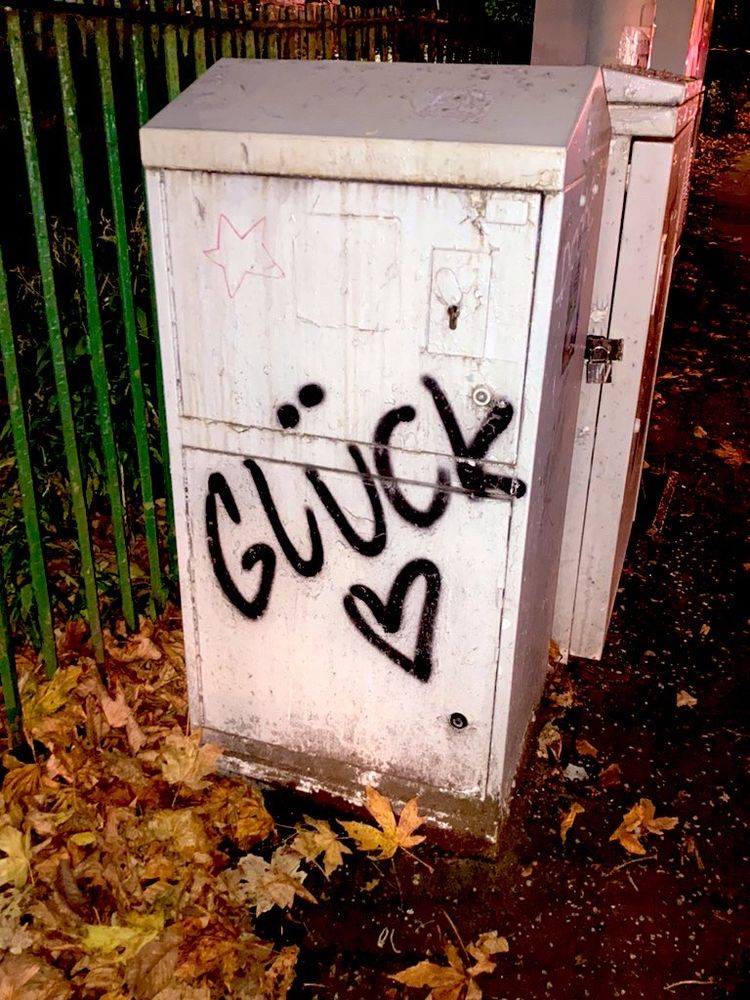 A piece of street furniture with the name Glück graffitied on it, with a heart sprayed underneath
