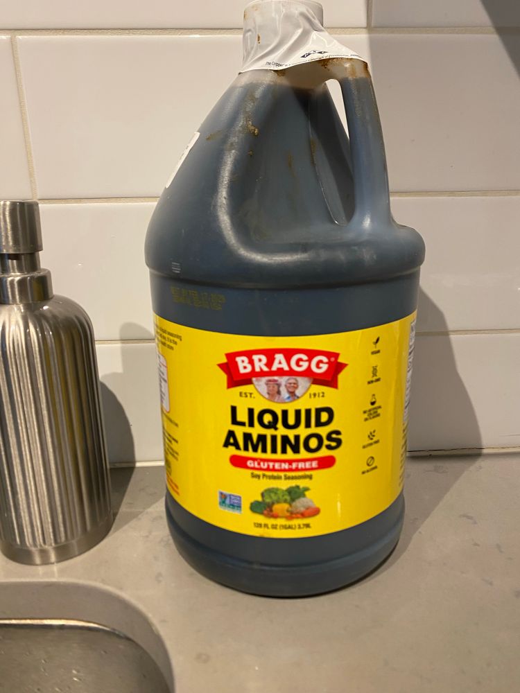 I seemingly gigantic one-gallon jug of Bragg’s Liquid Aminos, next to a kitchen soap dispenser to give the gallon jug scale. 