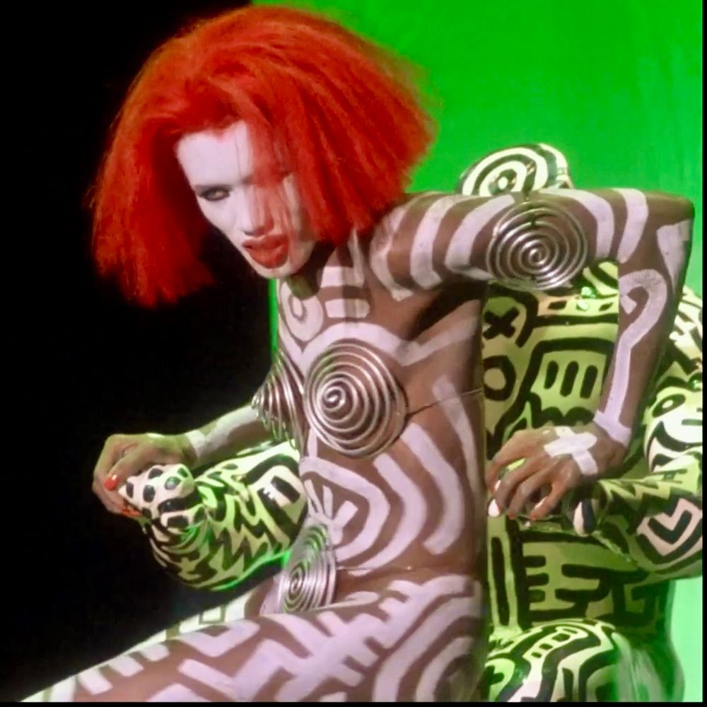 From the 80’s horror movie Vamp, Grace Jones in her famous Keith Haring-designed costume. Jones is wearing a revealing wire spiral bikini, and her body is hand-painted with white stripes & designs. 