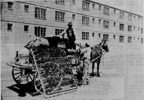 Two men tend to a horse-drawn cart loaded with personal effects in front of a pristine apartment building