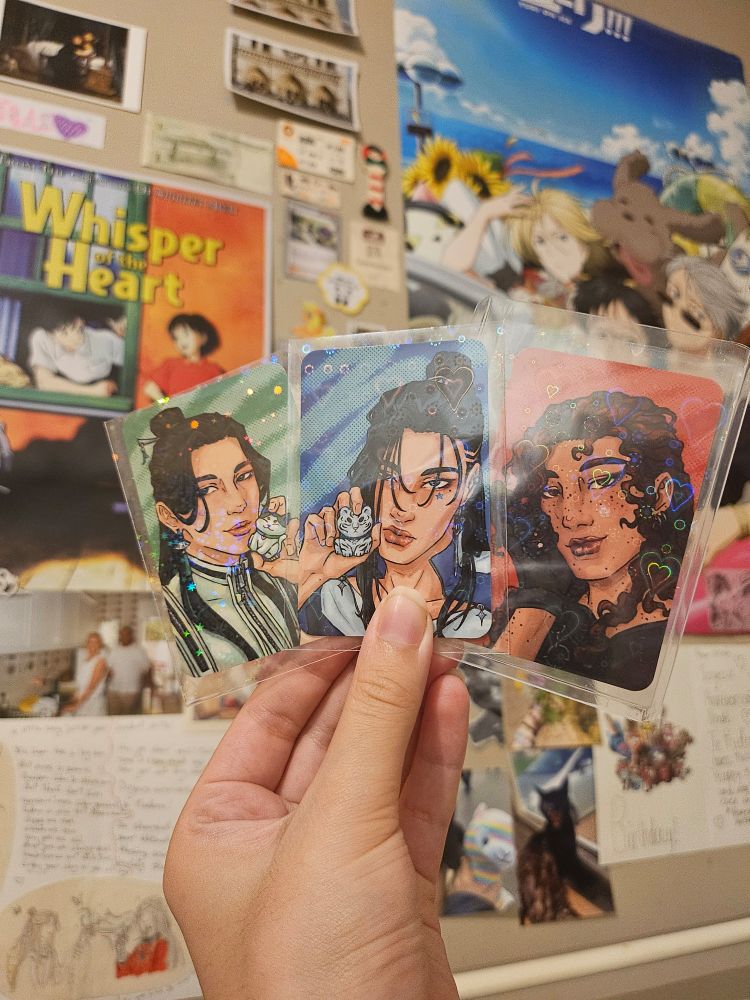 Another picture of my hand holding bingliushen photocards infront of a decorated wall background from a different angle to show the holographic designs on the photocard sleeves.