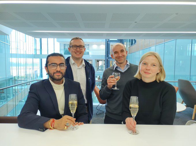 On the bottom left is Akaash Kumar, bottom right is Lara Kruger, behind lara is Manu Derivery and behind Akaash is James Manton, all holding glasses of champagne.