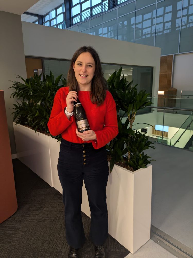 Picture of Julie wearing a red top and black bottoms, holding a bottle of champagne