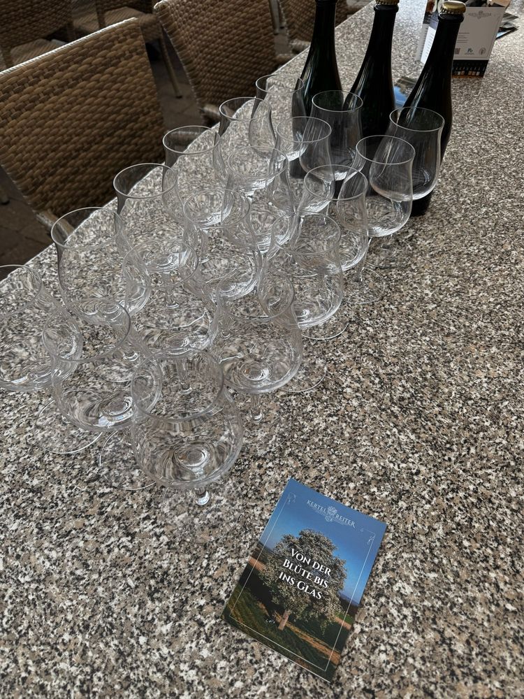 15 tasting glasses set out on a table with three bottles of cider and some flyers. 