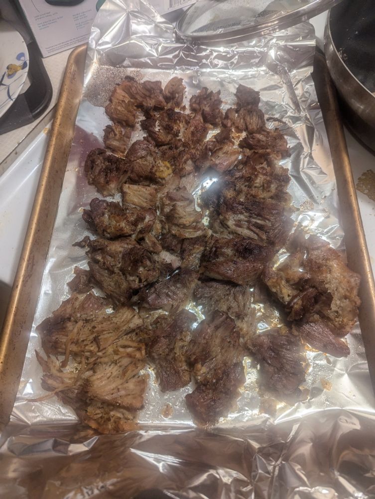 A foil-lined baking sheet with a bunch of nicely browned carnitas on it