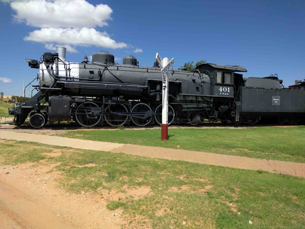 Steam engine on tracks before a blue sky. A few puffy clouds in the sky appear above the engine smoke stack making it look ready to go.