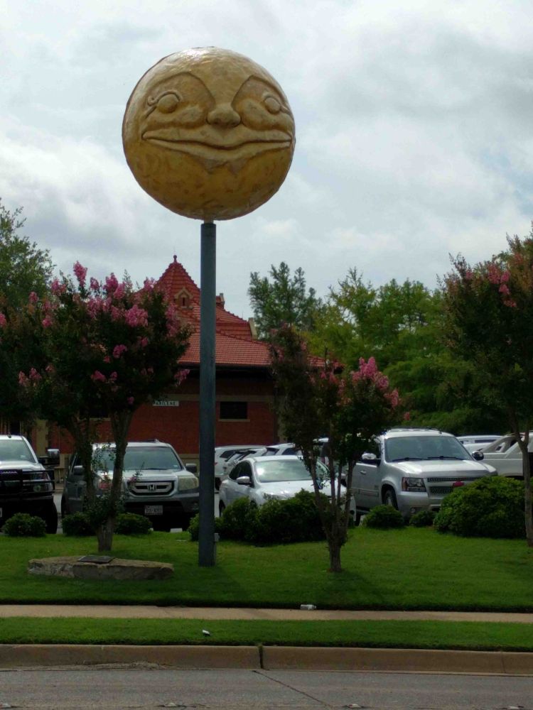 Sculpture of a full moon atop a pole. Moon has a smiling face.