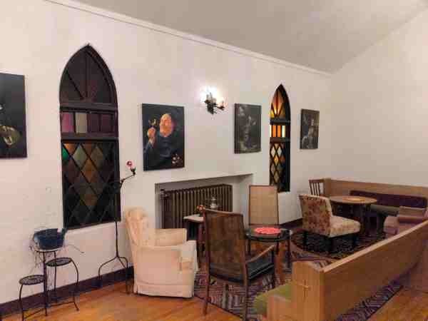 Interior of an old chapel, now a bar, with stained glass windows, portraits of monks, and comfy chairs.
