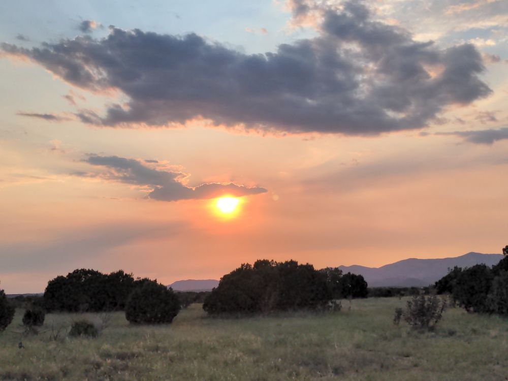 Sunset shows as an orange and yellow ball in a pink and orange sky due to smoke haze. A few dark clouds cut horizontally across the sky.