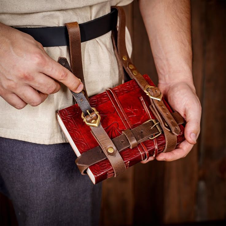 Photo of a leather book holster that hangs off a belt. https://www.tienda-medieval.com/de/baldrics/17737-leder-tagebuchhalter-zum-tragen-am-gurtel.html
