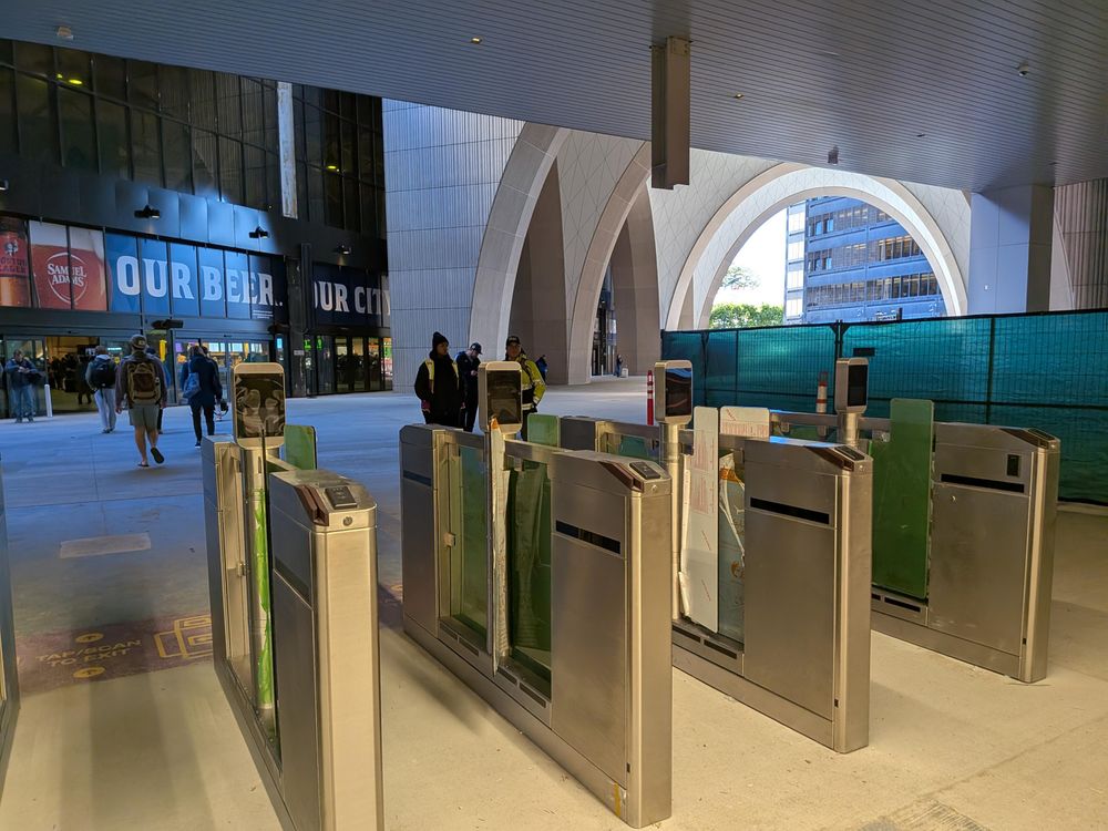 A row of slender dividers in the middle of a large, open concourse, each a few feet high. Retractable gates are visible, but all are locked in the open position, enabling unimpeded motion.