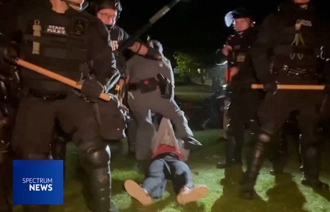 Screen grab of a news still showing a faculty member being dragged along the ground behind a line of riot police