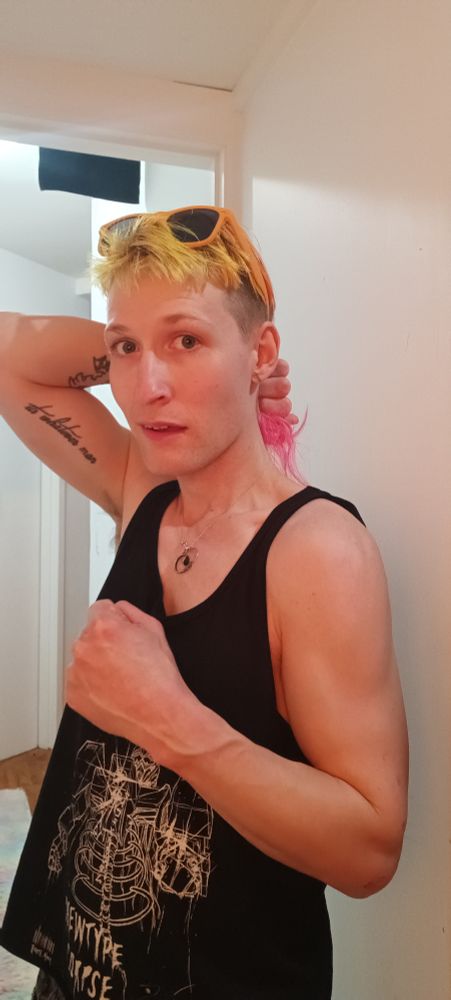 Kammy in a black tank-top that depicts a skeletal robot. It flexing one arm at its chest and holding another behind its head in a performative show of physique.