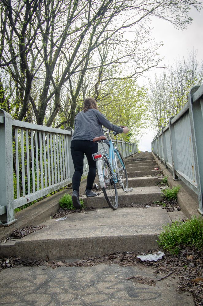 A bicyclist carries their bike up stairs. 