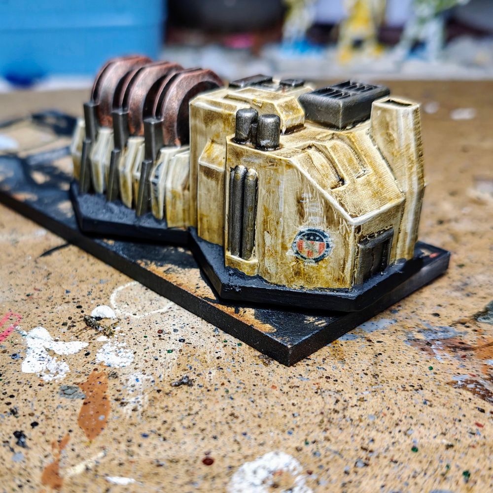 Side picture of a 6mm scale piece of terrain. The building is a power generator and has been painted mainly in kaki colour with metallic accents. The picture focuses on the Capitol symbol