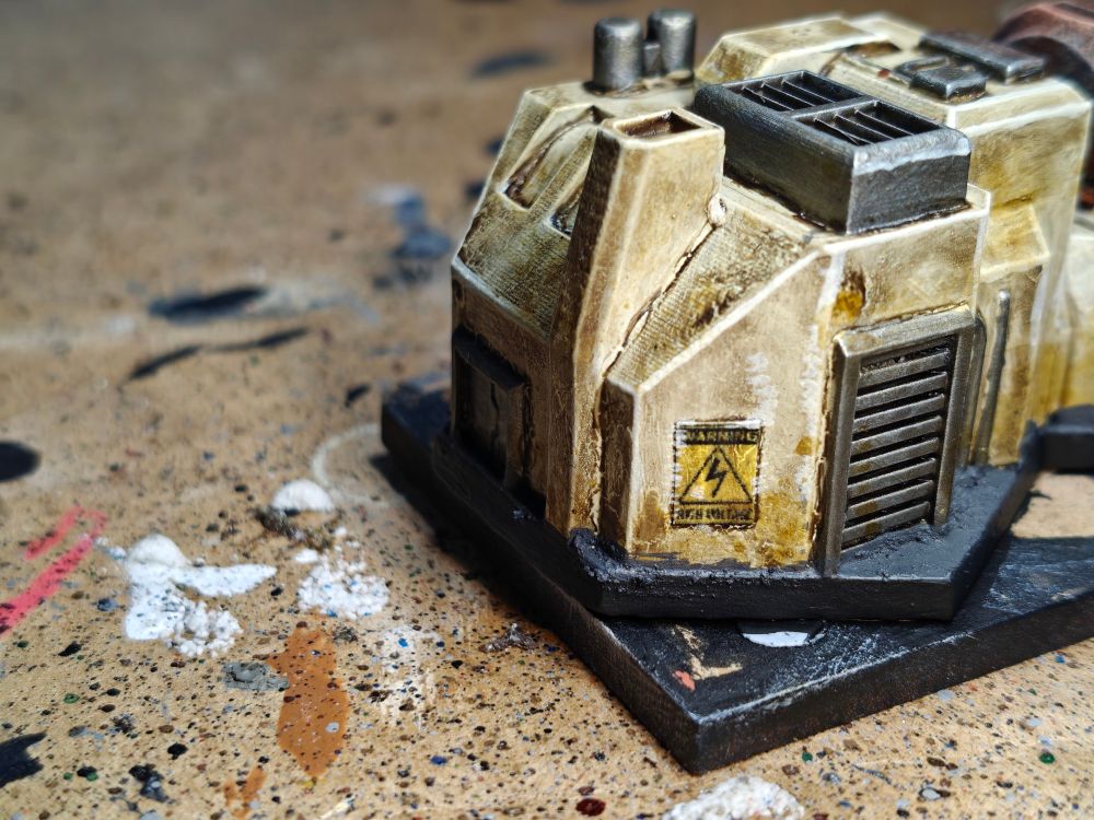 A detail of a 6mm scale piece of terrain. The detail shows a High Voltage warning poster. The building is a power generator and has been painted mainly in kaki colour with metallic accents.