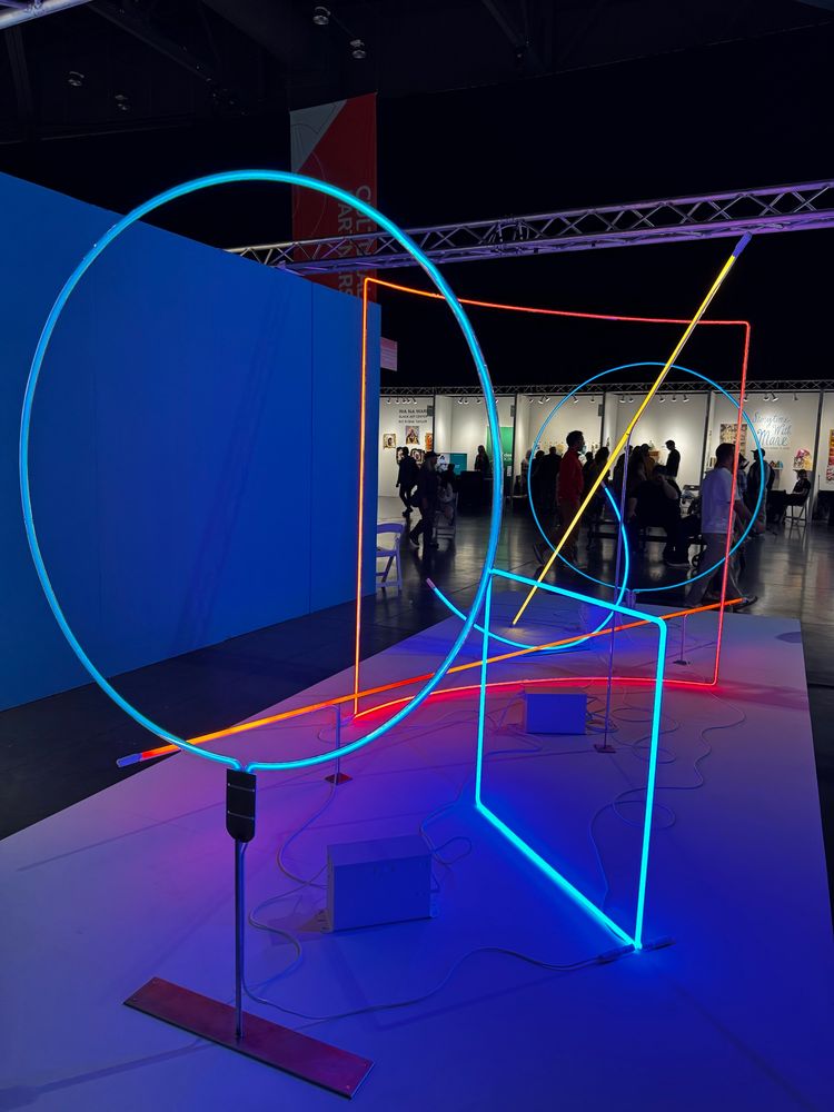 A neon light installation comprising various noble gas colors in simple shapes like circles, lines, and squares. 