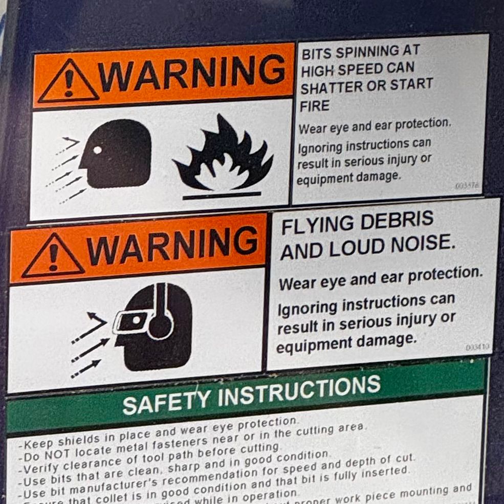 A spate of machinery-related safety warnings, including "FLYING DEBRIS AND LOUD NOISE" and "BITS SPINNING AT HIGH SPEED CAN SHATTER OR START FIRE". Also, highly stylized cartoon faces with many arrows pointing at them.