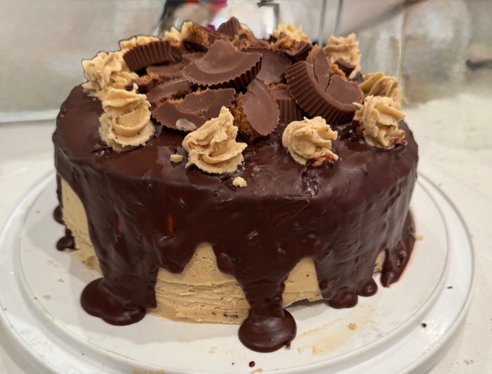 A peanut butter and chocolate cake. The frosting is peanut butter with a chocolate ganache drizzle and it is topped with peanut butter cups 