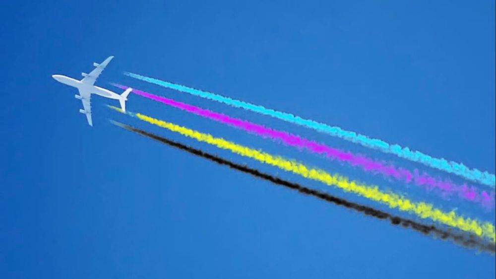 A photo looking up at a jet in the sky flying past and it has four contrails behind in the colours cyan magenta yellow and black.