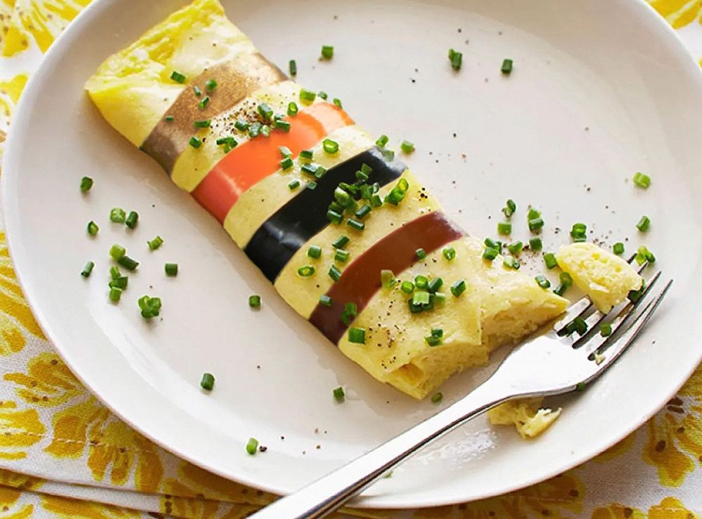 A foodie style photo of an omelette on a plate with a fork having just taken a piece out, sprinkled with fresh chives, and with four bands of colour across the omelette; brown, black, orange, and gold. The bands of colour are those used on resistors; hence, an ohmelette.