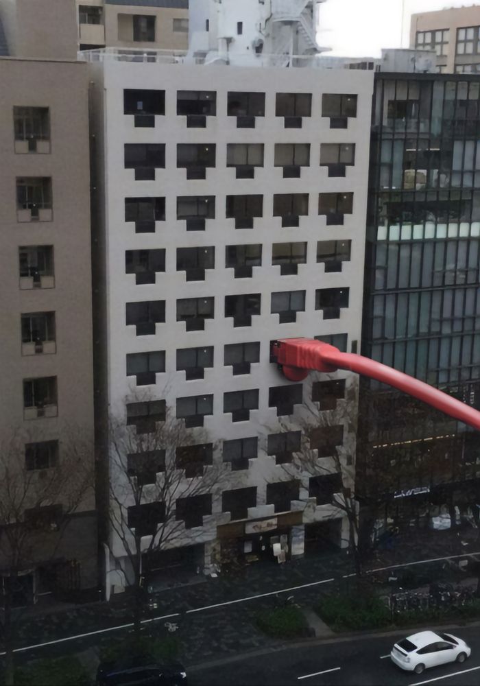 A photo of a building with windows that look vaguely similar to an ethernet or other RJ port. In one window is plugged a giant red ethernet cable hammering the point home like a joke explained too far.