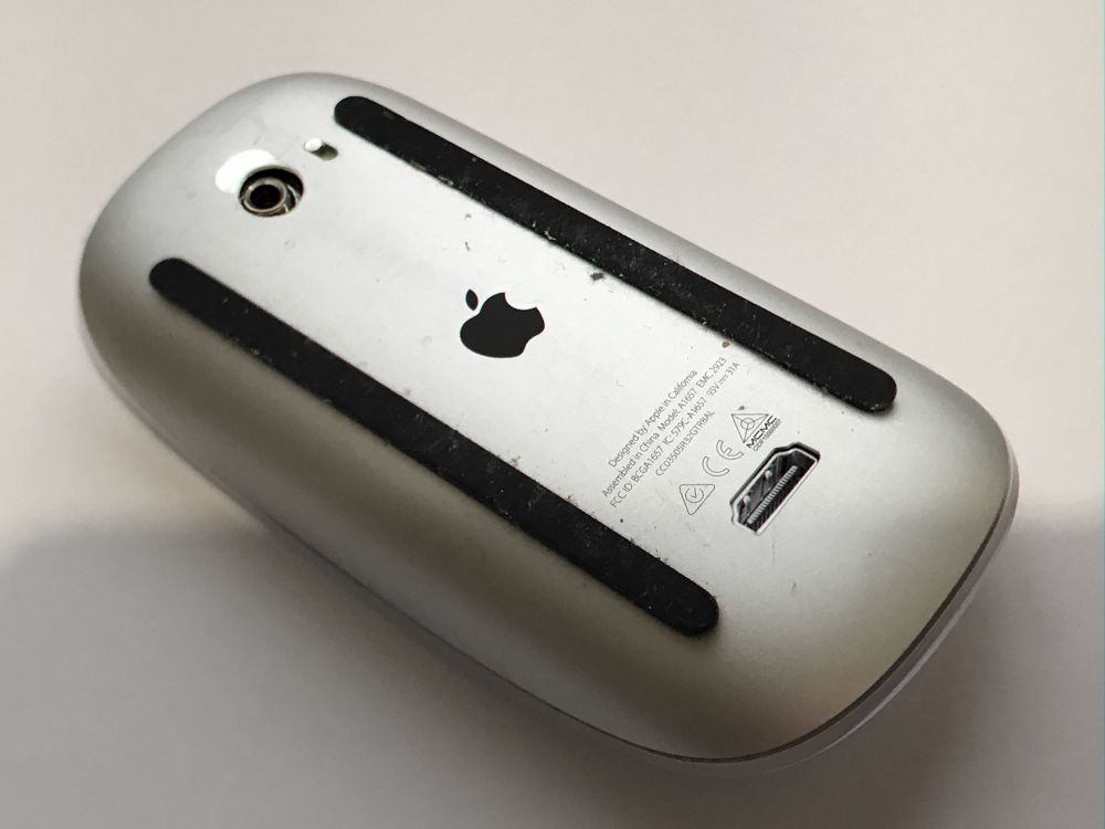 A picture of an Apple mouse upside down on a desk, its ports in the air. It's on a white background, its shiny aluminium body still. It could be scared, it could be resting. You know what you have to do.
