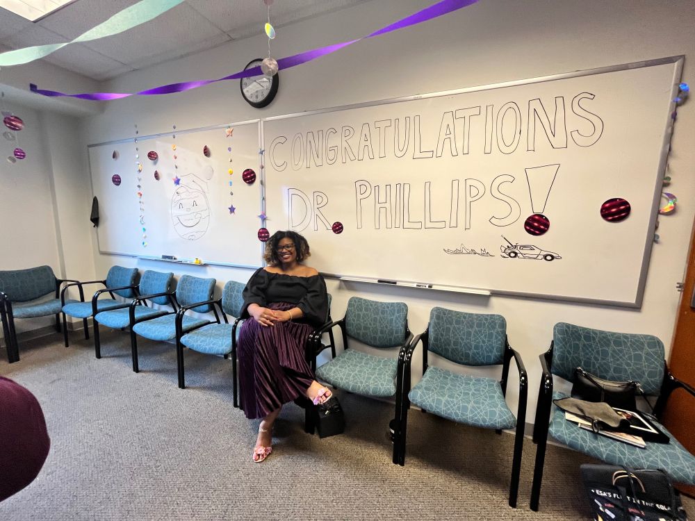 Caprice in front of a white board that reads - Congratulations Dr. Phillips