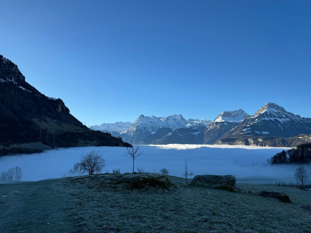 Looking down on clouds / fog with blue sky and mountains in the background.