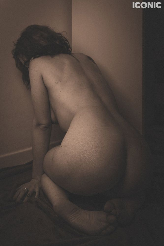 Vintage toned professional photo of a naked person showing their back, kneeling next to a wall, hiding their face