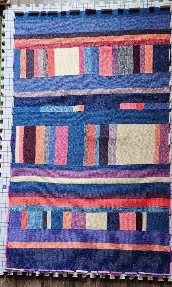 Knit blanket with stripes and blocks of color going in multiple directions. Blues and purples and oranges and creams are dominant colors.