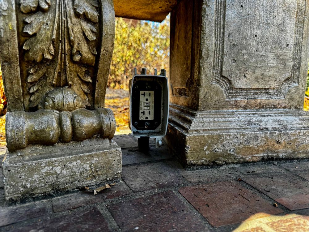 A forgotten outlet gasps for relevance beneath the weight of time, its open mouth silently pleading for a purpose long since abandoned. Stone pillars, carved with care by hands now dust, loom in indifference. The golden decay of autumn mocks the illusion of permanence.