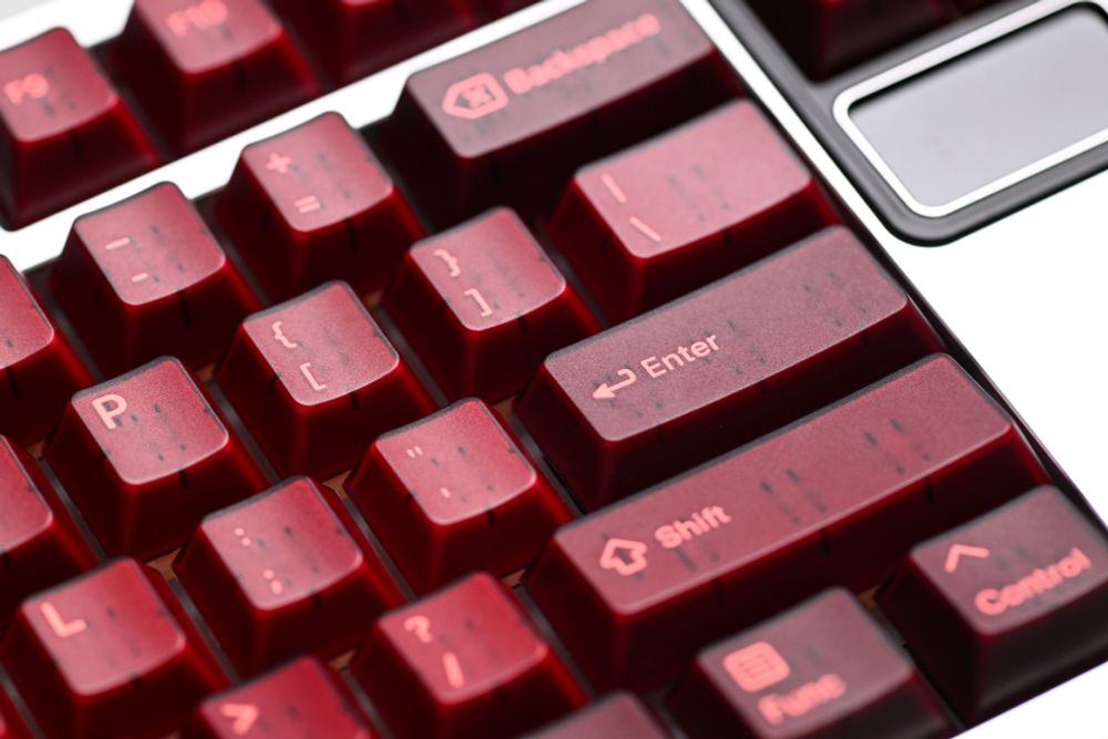 A close-up shot of part of a mechanical keyboard showing several translucent maroon keycaps, on a silver keyboard