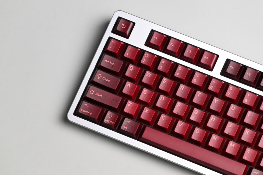 An angled shot of a mechanical keyboard showing translucent maroon keycaps, on a silver keyboard