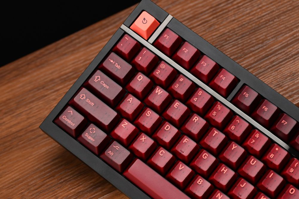 A close-up shot of part of a mechanical keyboard showing a bright pink escape key, and other translucent maroon keycaps, on a black keyboard