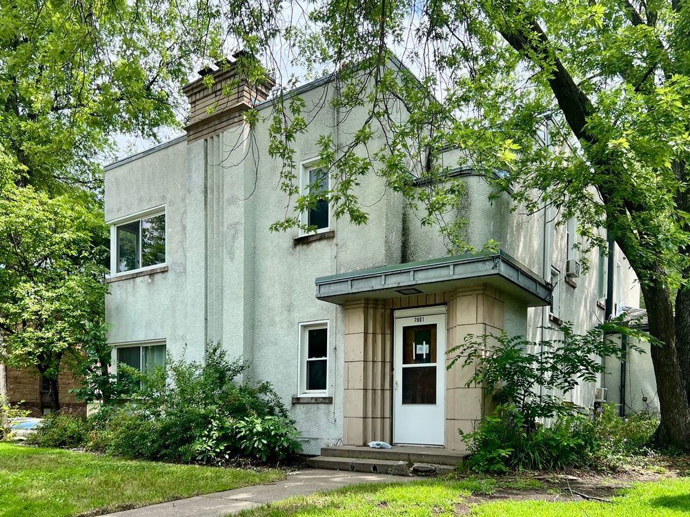 Boxy stucco duplex with a fluted chimney, recessed doorway, and stepped walls above the entrance.