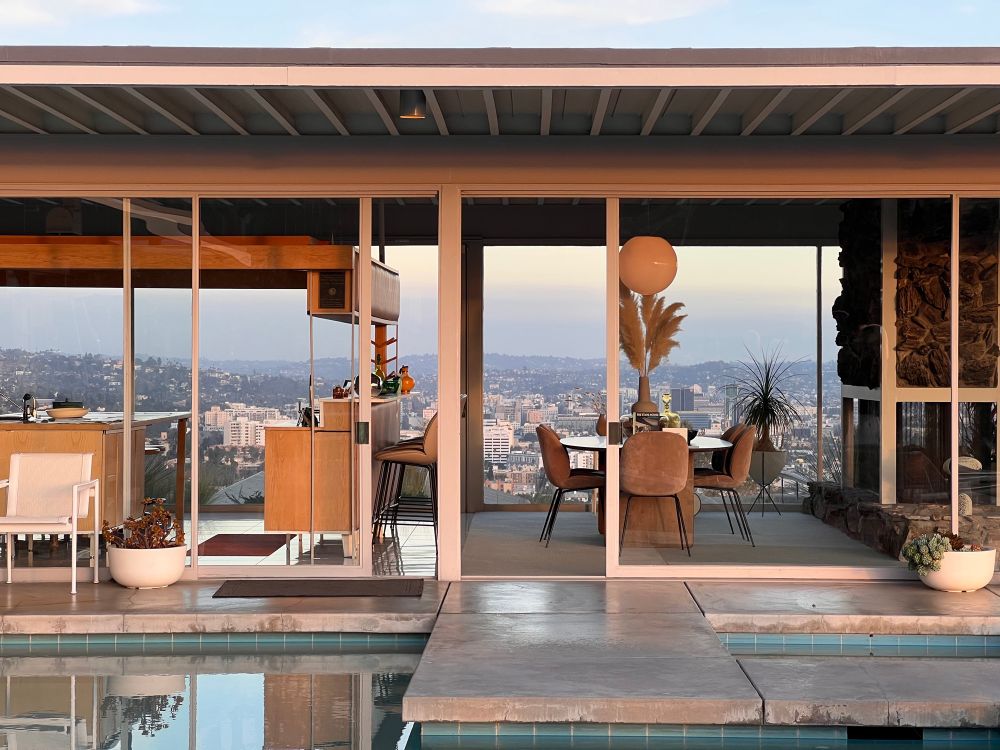 A view directly through the kitchen and dining room of the house as seen from the pool. The Hollywood Hills and Los Angeles can be seen on the other side of the house through the glass walls.