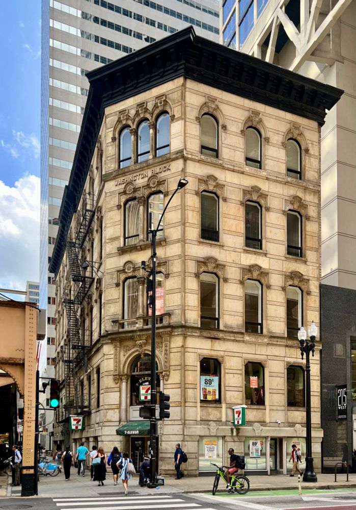A five-story limestone Italianate building with a chamfered corner, surrounded by skyscrapers.