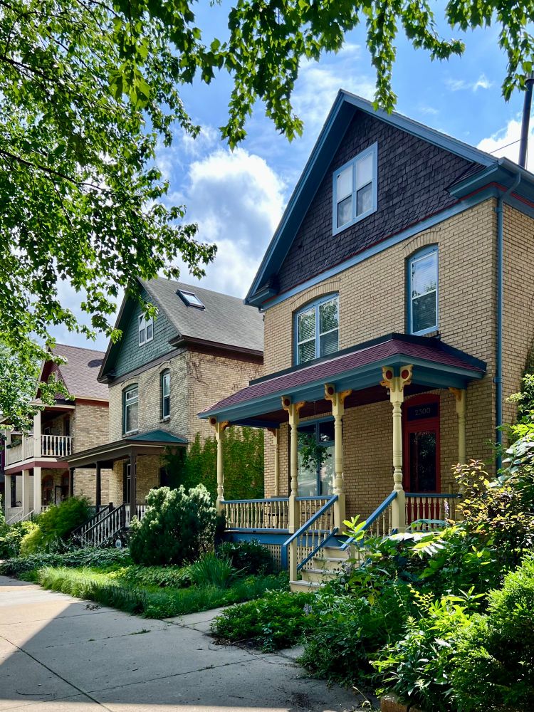 Row of front gabled brick houses in a row with lots of greenery.