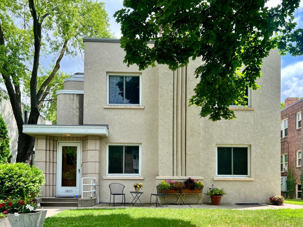 Boxy stucco duplex with a fluted chimney, recessed doorway, and stepped walls above the entrance.